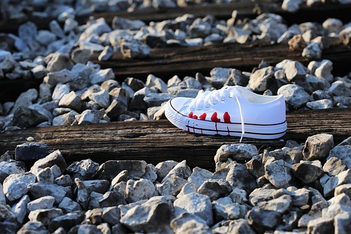 a white sneaker with red stains at its side on a log surrounded by pebbles