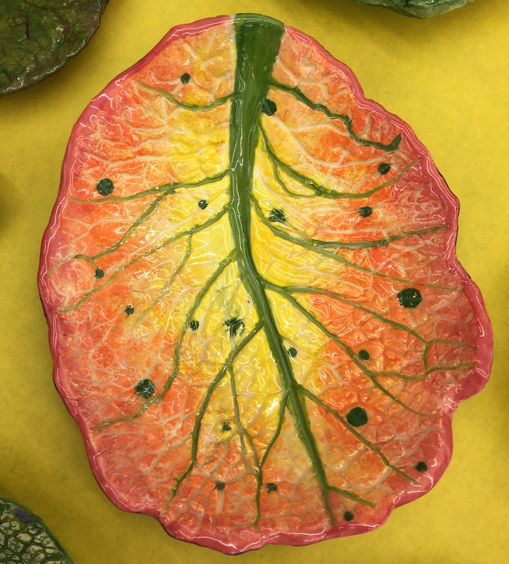 a leaf shaped ceramic plate with leaf veins idented, the stem is colored in green while the plate is colored from yellow at the center gradiates to red at the edges. The smaller veins are left in white.