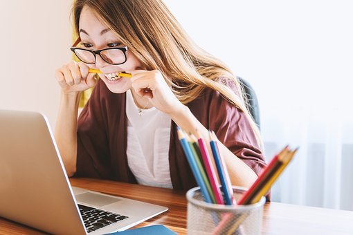 a woman sitting in front of a computer and biting a pencil in frustration
